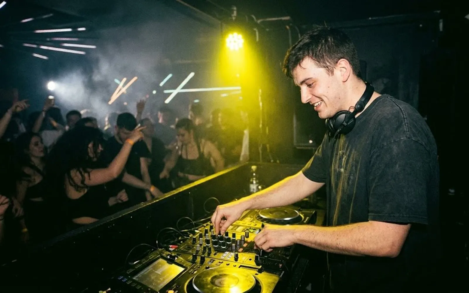 Uśmiechnięty DJ gra swój set przed tańczącą publiką w zadymionym klubie