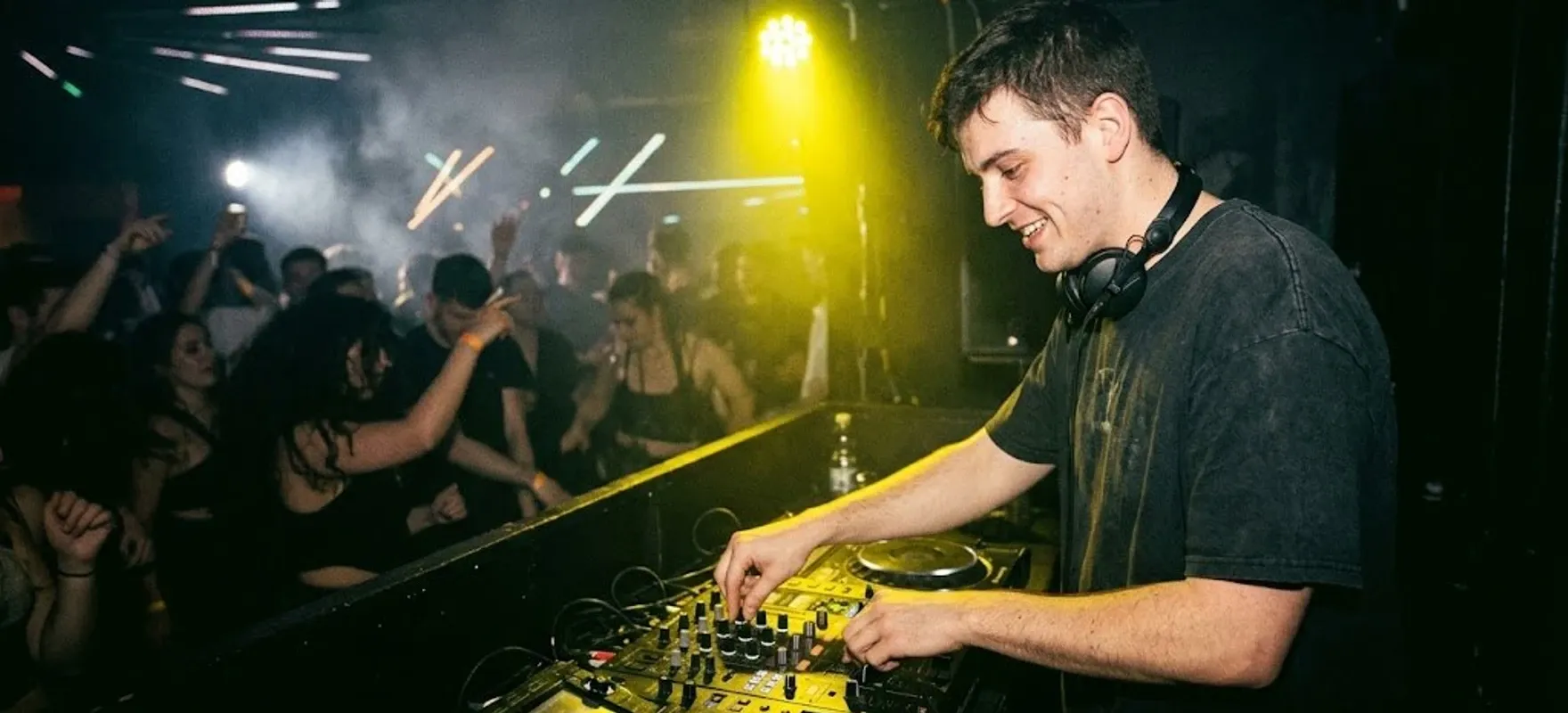 Uśmiechnięty DJ gra swój set przed tańczącą publiką w zadymionym klubie